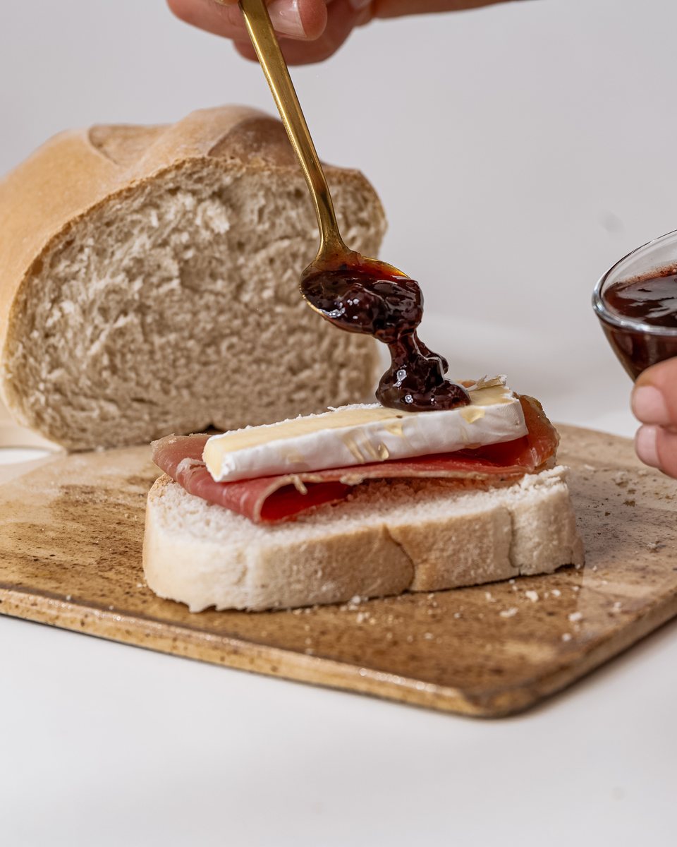 Mermelada servida sobre un sándwich de pan casero, jamón crudo y queso brie